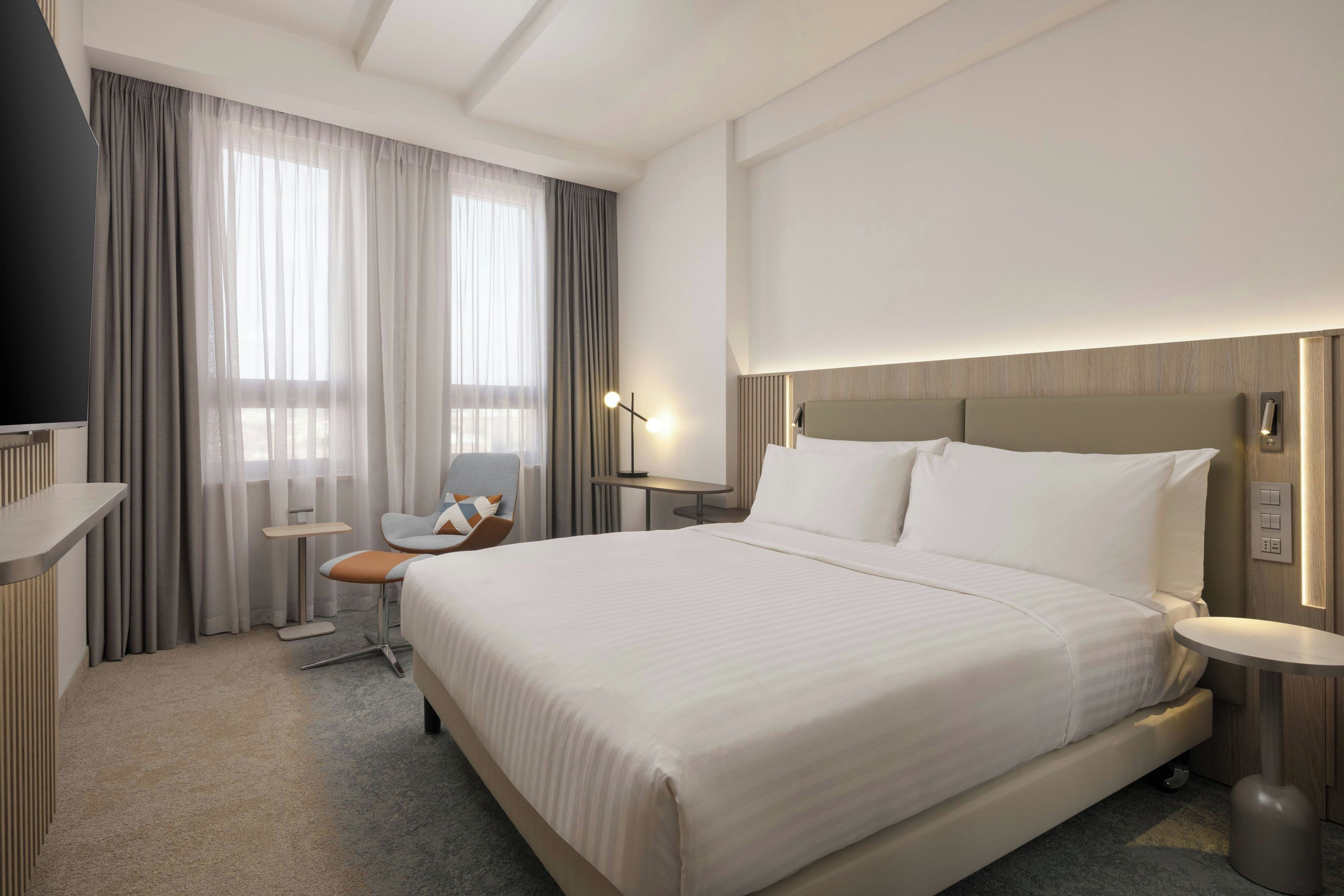 A hotel room with a large bed, a chair, a desk, and a TV.
