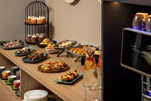 Una mesa de buffet con diversos alimentos y una pantalla de televisión al fondo.