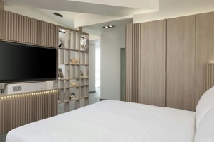 Un dormitorio moderno con una cama grande, un televisor y estanterías empotradas con objetos decorativos.