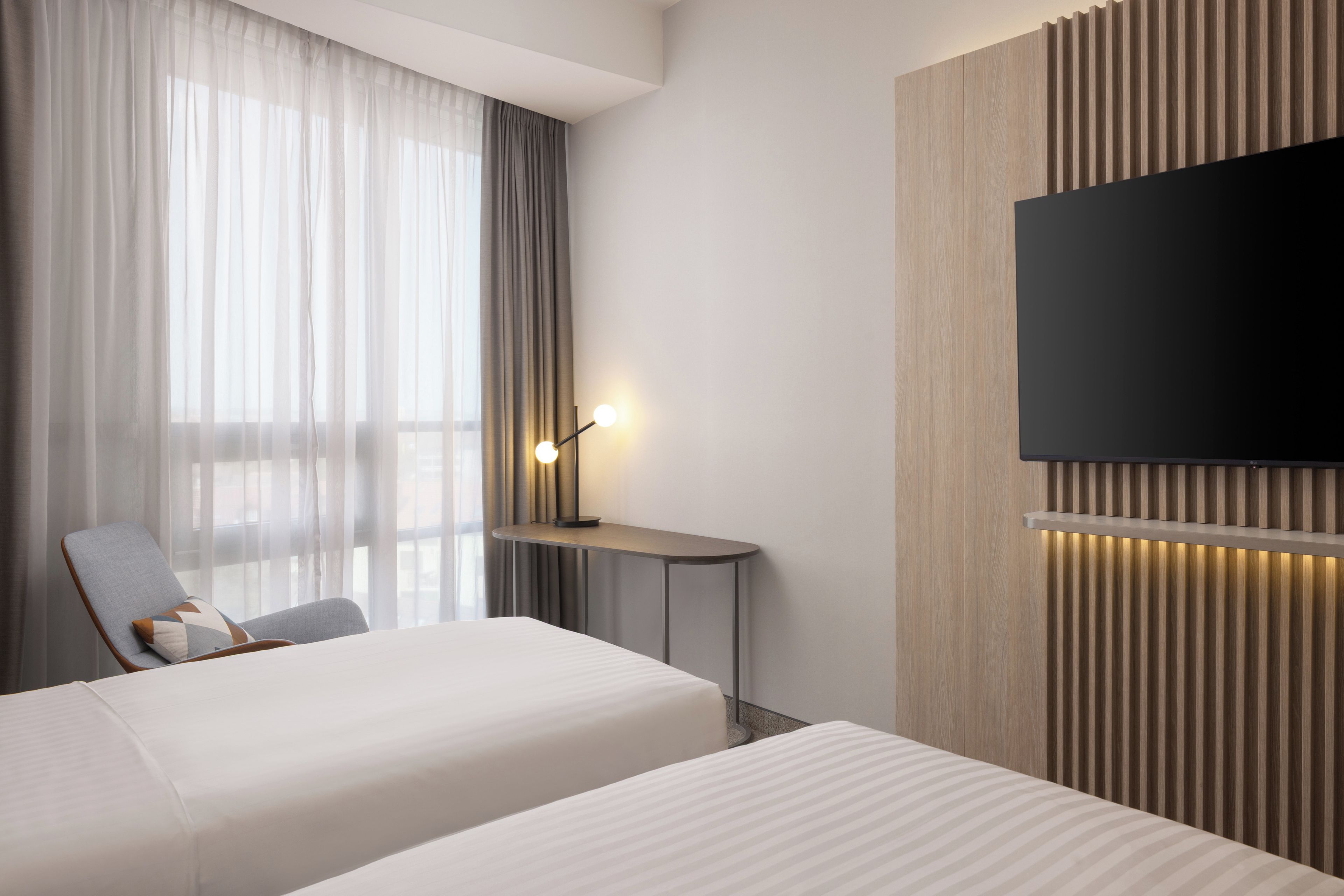 A hotel room with a bed, a desk, a chair, a TV, and a window with curtains.