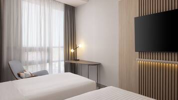 Una camera d'albergo con un letto, una scrivania, una sedia, una televisione e una finestra con tende.