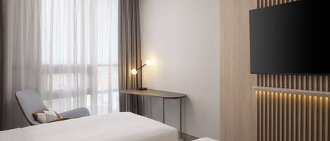 A hotel room with a bed, a desk, a chair, a TV, and a window with curtains.