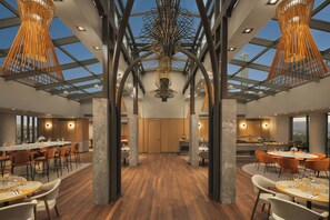 A modern dining area with high ceilings, exposed beams, and a central chandelier. Tables are set for dining with chairs. - Courtyard by Marriott Downtown Sibiu (Sibiu)