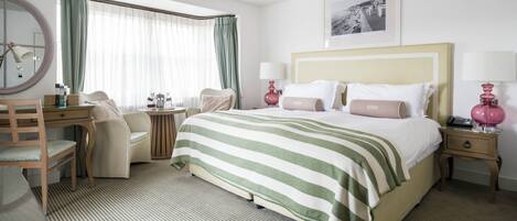 Quarto de hotel com cama, mesas de cabeceira, escrivaninha, cadeira, espelho e janela com cortinas.