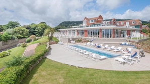 A large building with a swimming pool and sun loungers.