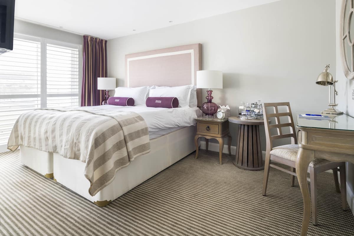 Une chambre d’hôtel avec un grand lit, deux tables de chevet, un bureau avec une chaise et une fenêtre avec des rideaux.