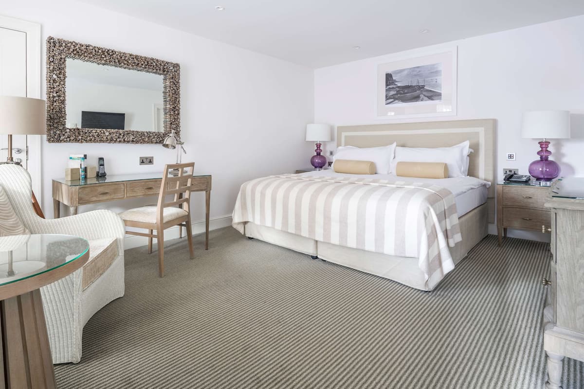 Une chambre d’hôtel avec un lit, une chaise, un bureau, une commode et un miroir.