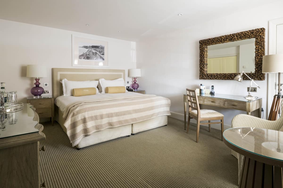 Une chambre d’hôtel comprenant un lit, des tables de chevet, un bureau, une chaise et un grand miroir.