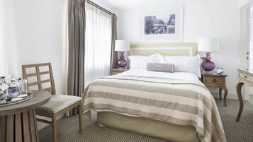 A hotel room with a bed, two bedside tables, a chair, a small table with a tray, and a window with curtains.