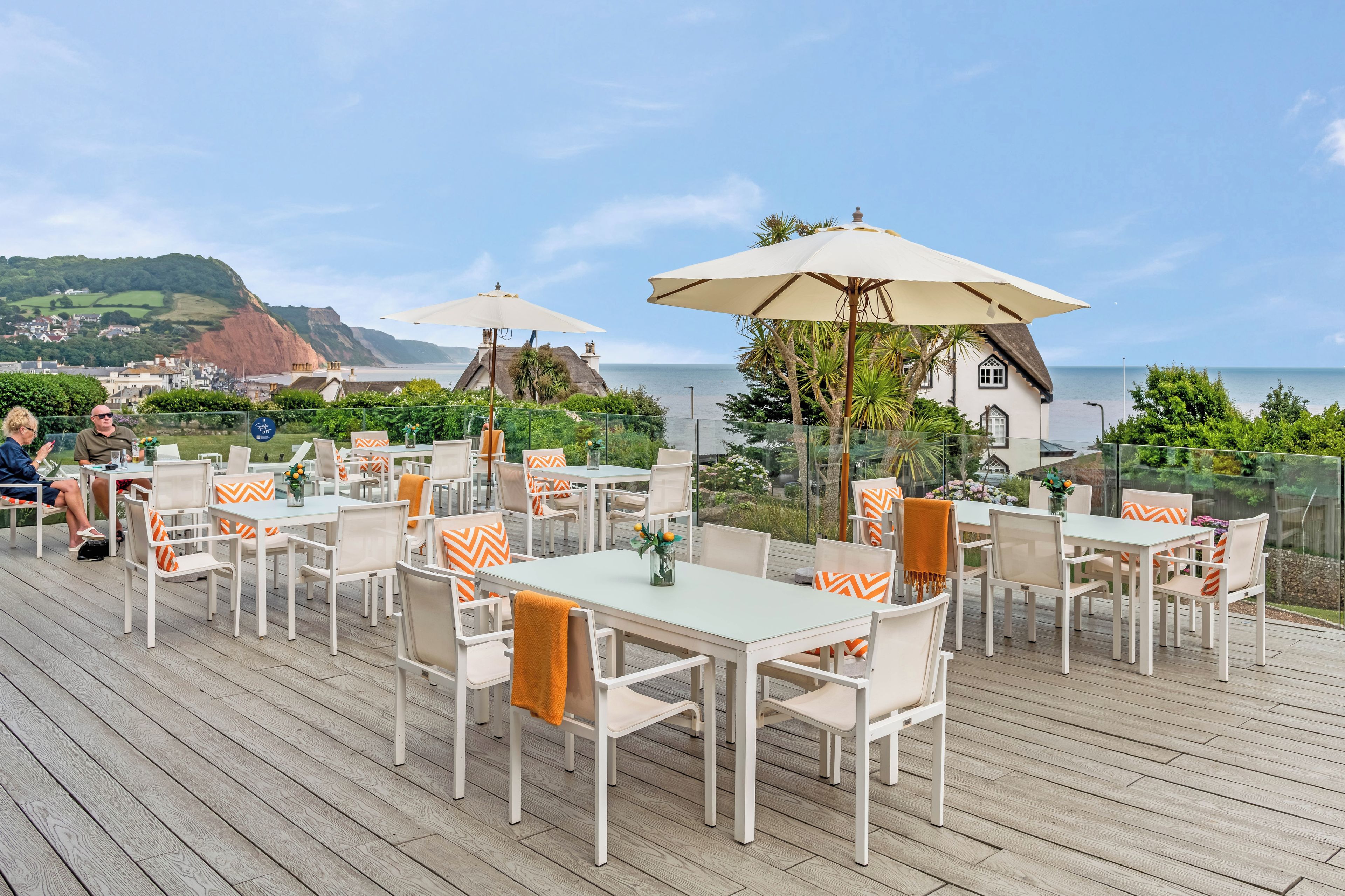 An outdoor dining area with tables and chairs, overlooking a coastal landscape.
