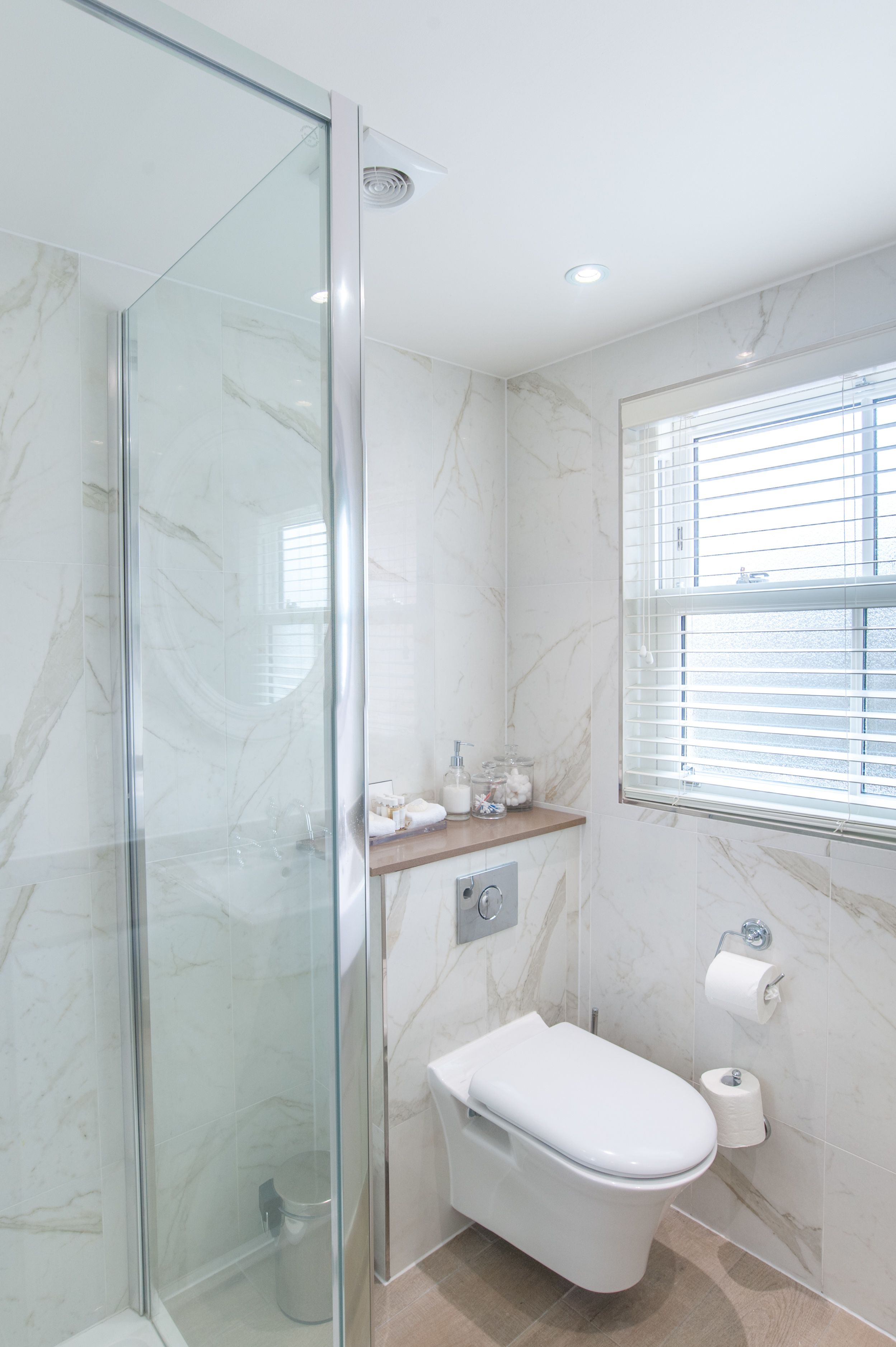 Un baño moderno con cabina de ducha de vidrio, inodoro y ventana con persianas.