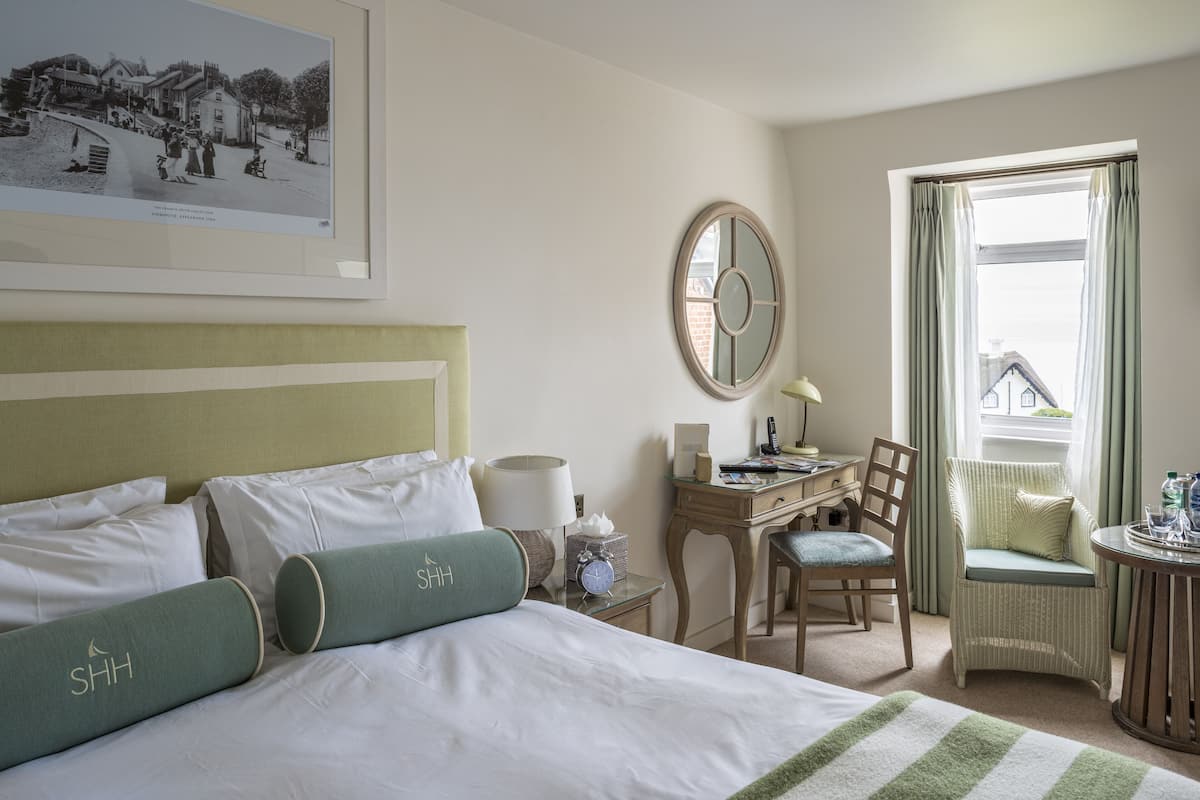 Une chambre d’hôtel avec un lit, un bureau, une chaise, une table ronde et une fenêtre avec des rideaux.