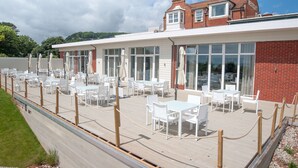 A seaside restaurant with outdoor seating, a brick building, and a view of the sea.