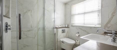 Ein modernes Badezimmer mit einer gläsernen Dusche, einer Toilette und einem Waschbecken mit Marmorplatte.