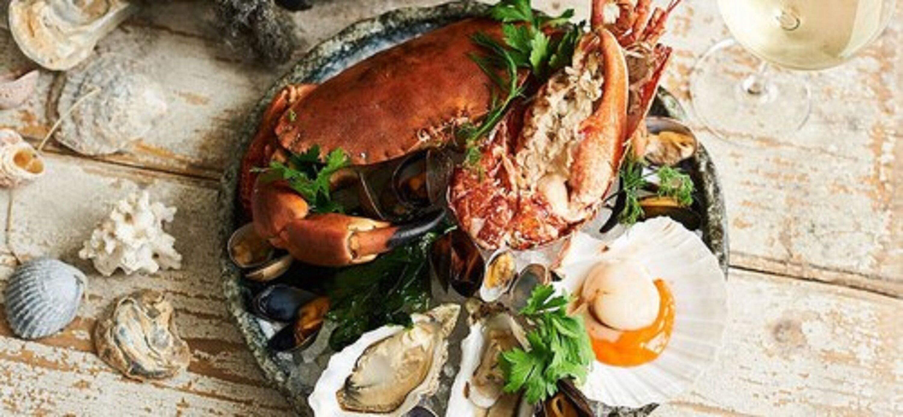 Un plateau de fruits de mer comprenant un crabe, des moules, des palourdes et une noix de Saint-Jacques, présenté sur une table en bois rustique.