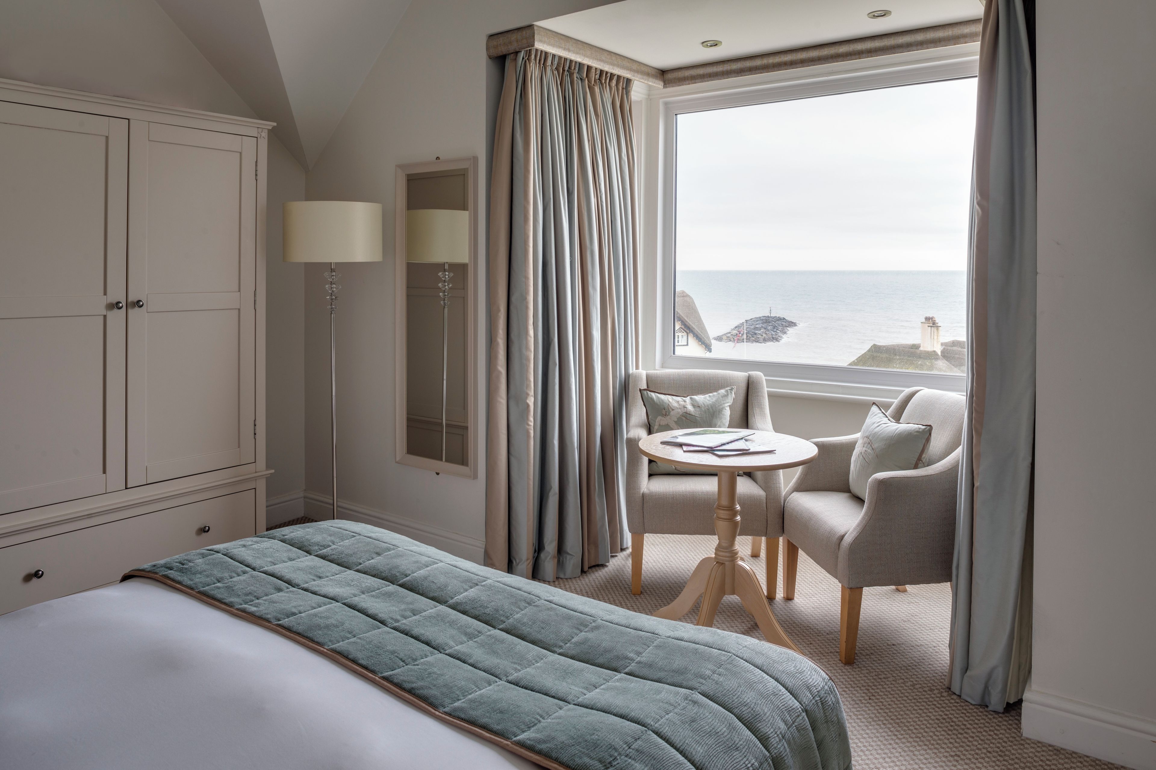 A hotel room with a bed, a seating area with a table, and a view of the sea.