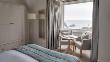 A hotel room with a bed, a seating area with a table, and a view of the sea.