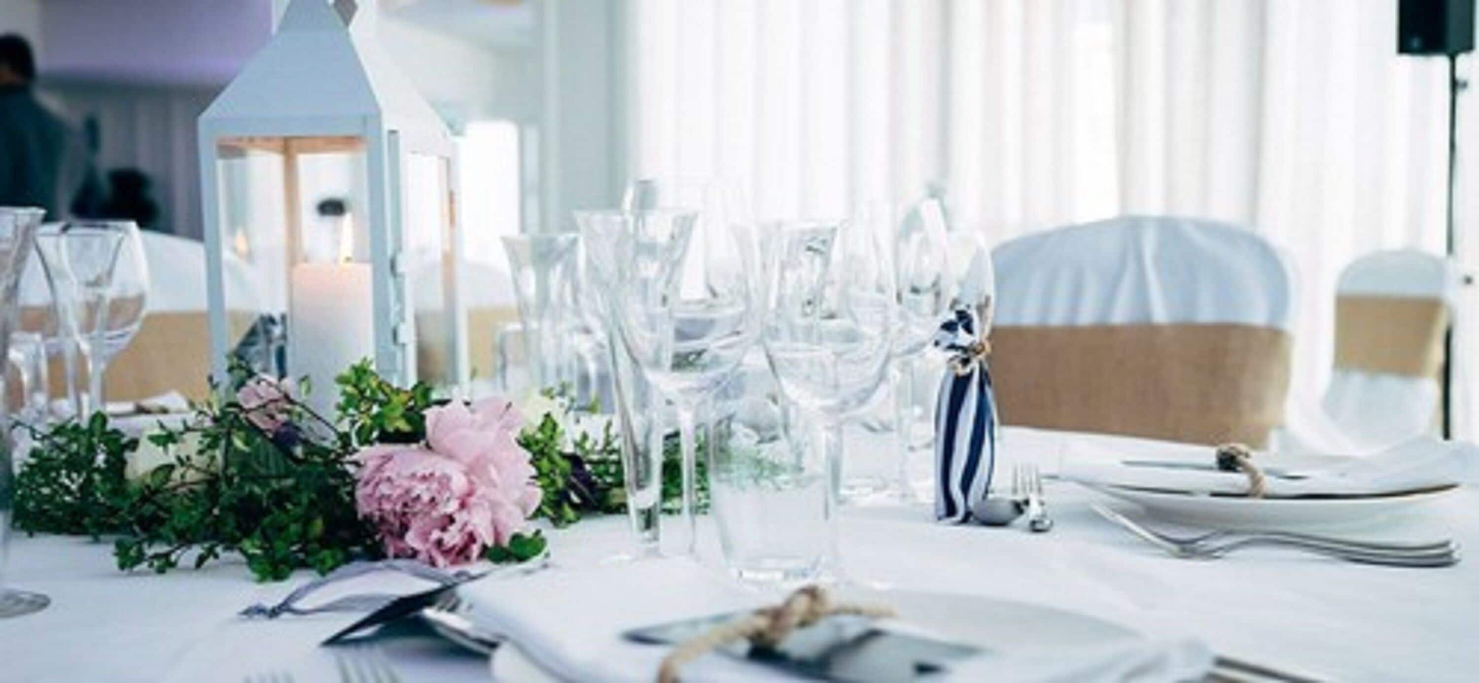 Mesa dispuesta para un evento formal con cristalería transparente, una vela y un centro de mesa floral.