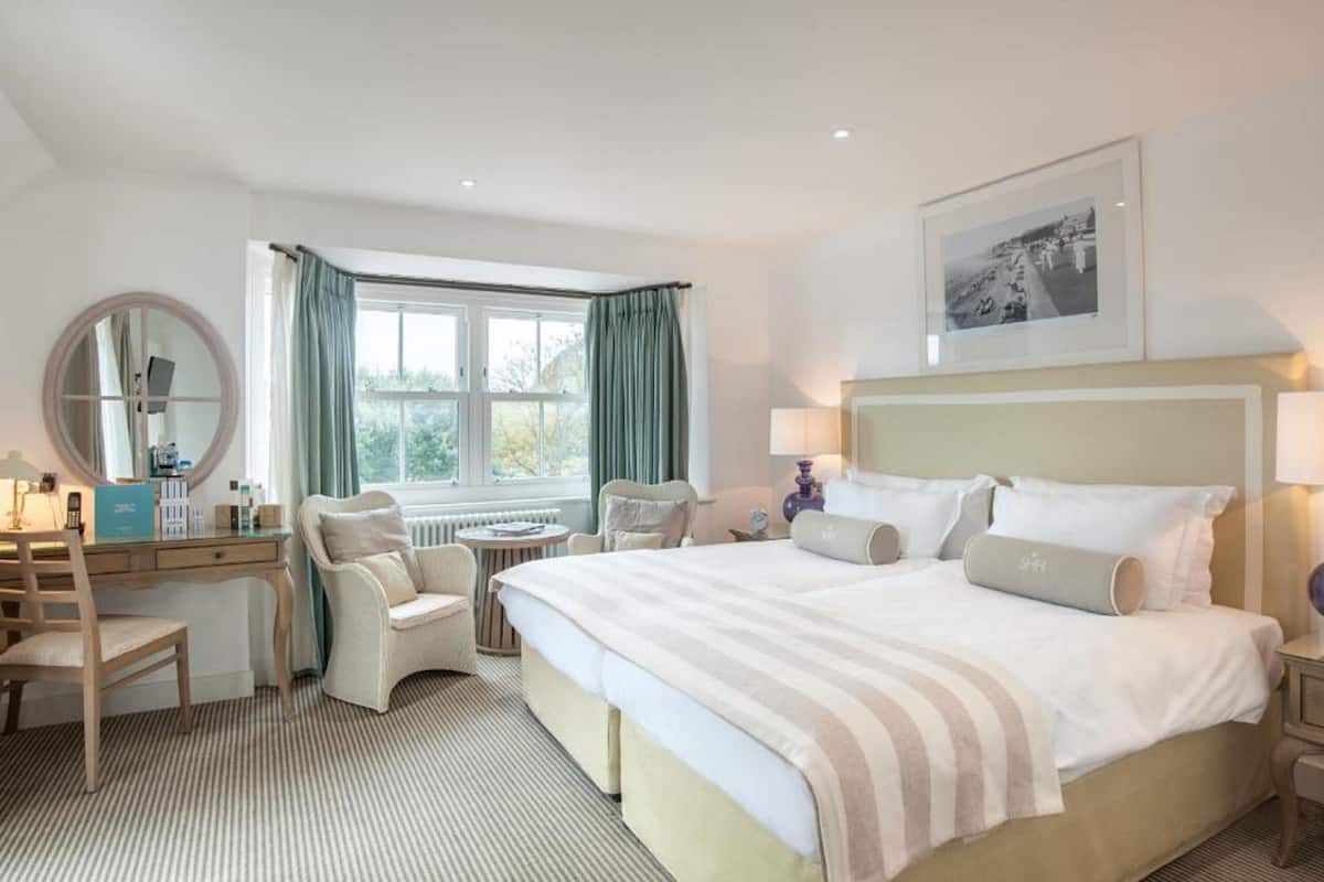 Une chambre d’hôtel avec un grand lit, un bureau avec une chaise, un miroir rond et une fenêtre avec des rideaux.