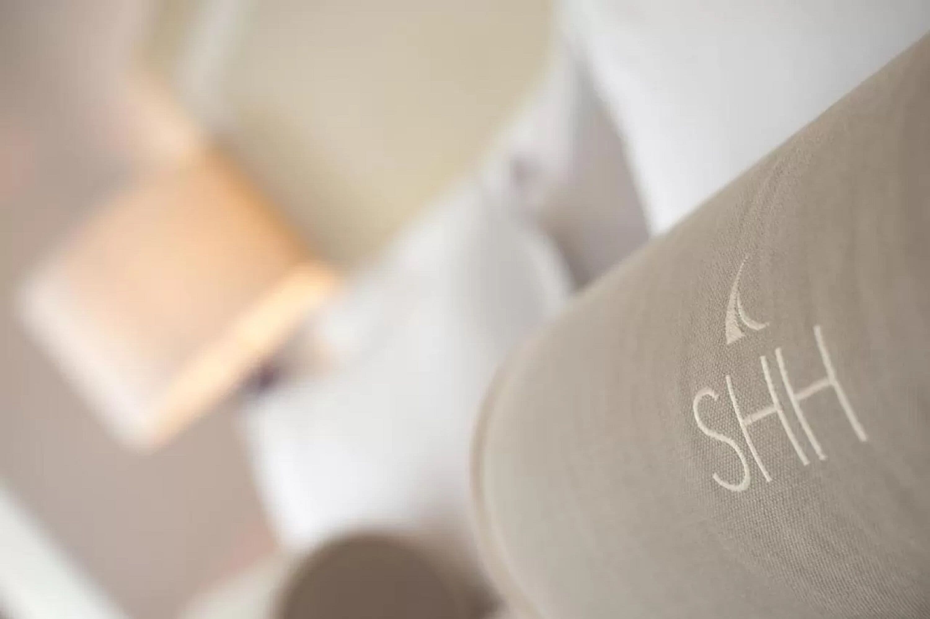 A close-up of a white fabric with the letters "SHH" embroidered on it.