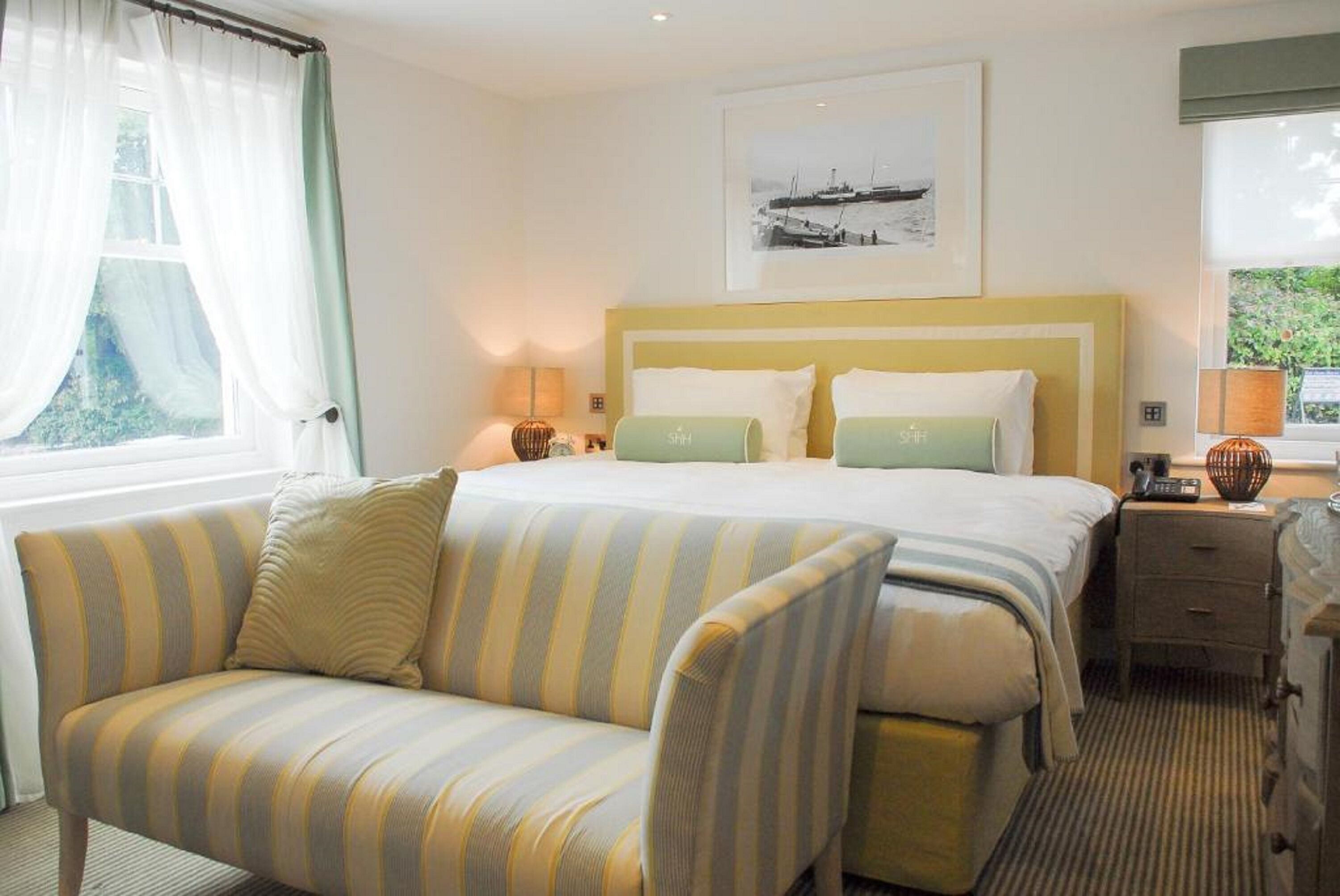 Una habitación de hotel con cama, sofá, mesita de noche y ventana con cortinas.