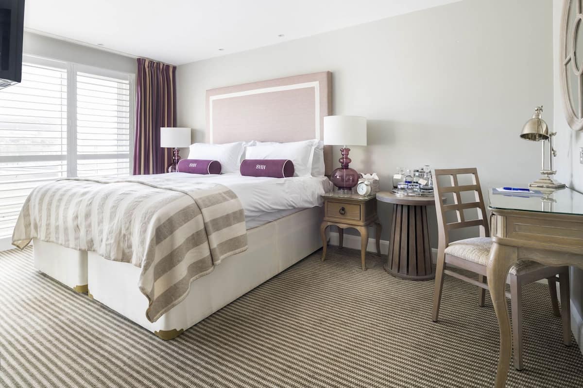 Une chambre d’hôtel avec un lit, des tables de chevet, une chaise, un bureau et une fenêtre.
