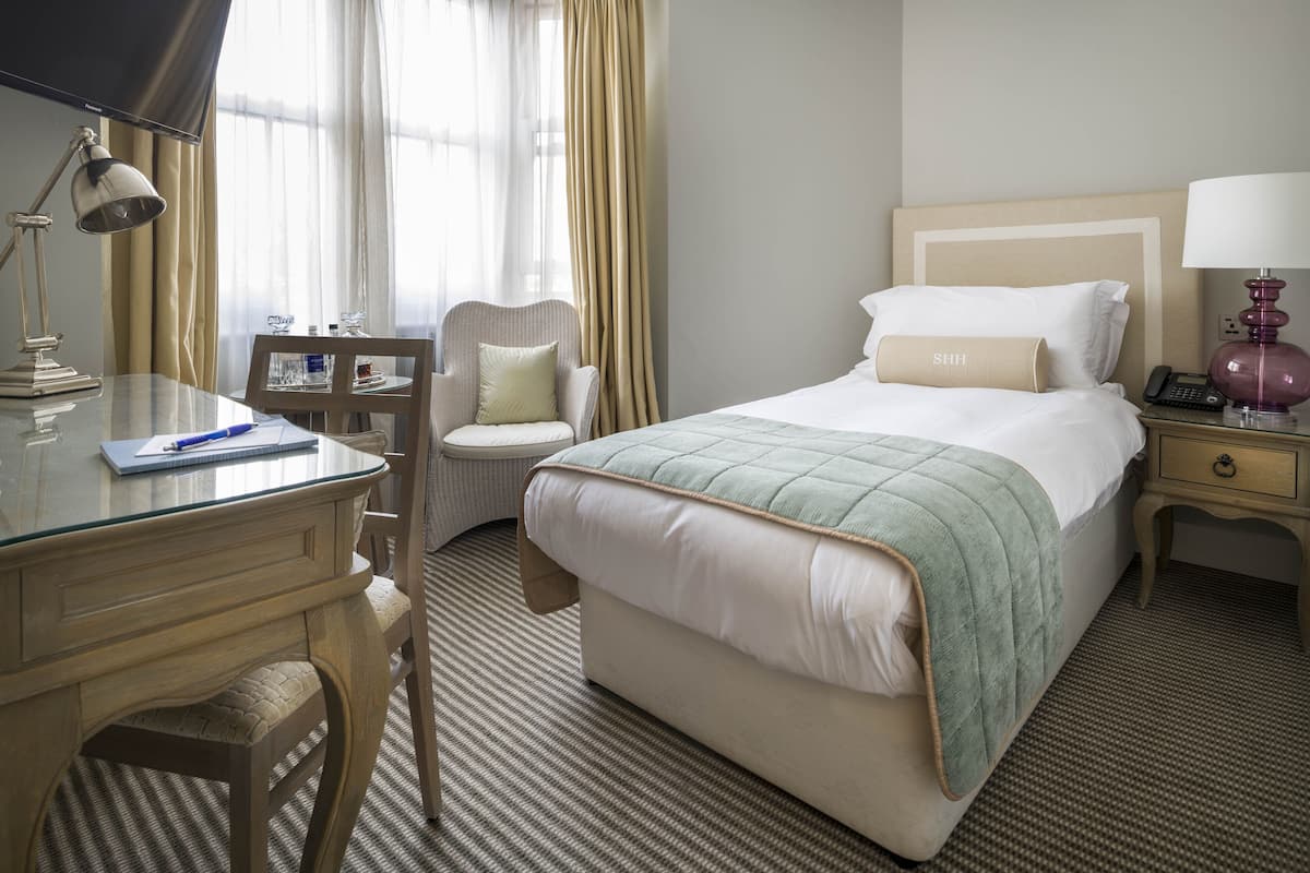 Une chambre d’hôtel avec un lit, un bureau avec une lampe, une chaise et une table de chevet avec un téléphone.