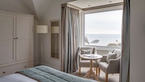 A hotel room with a bed, a seating area with a table and chairs, a wardrobe, a lamp, and a view of the sea.
