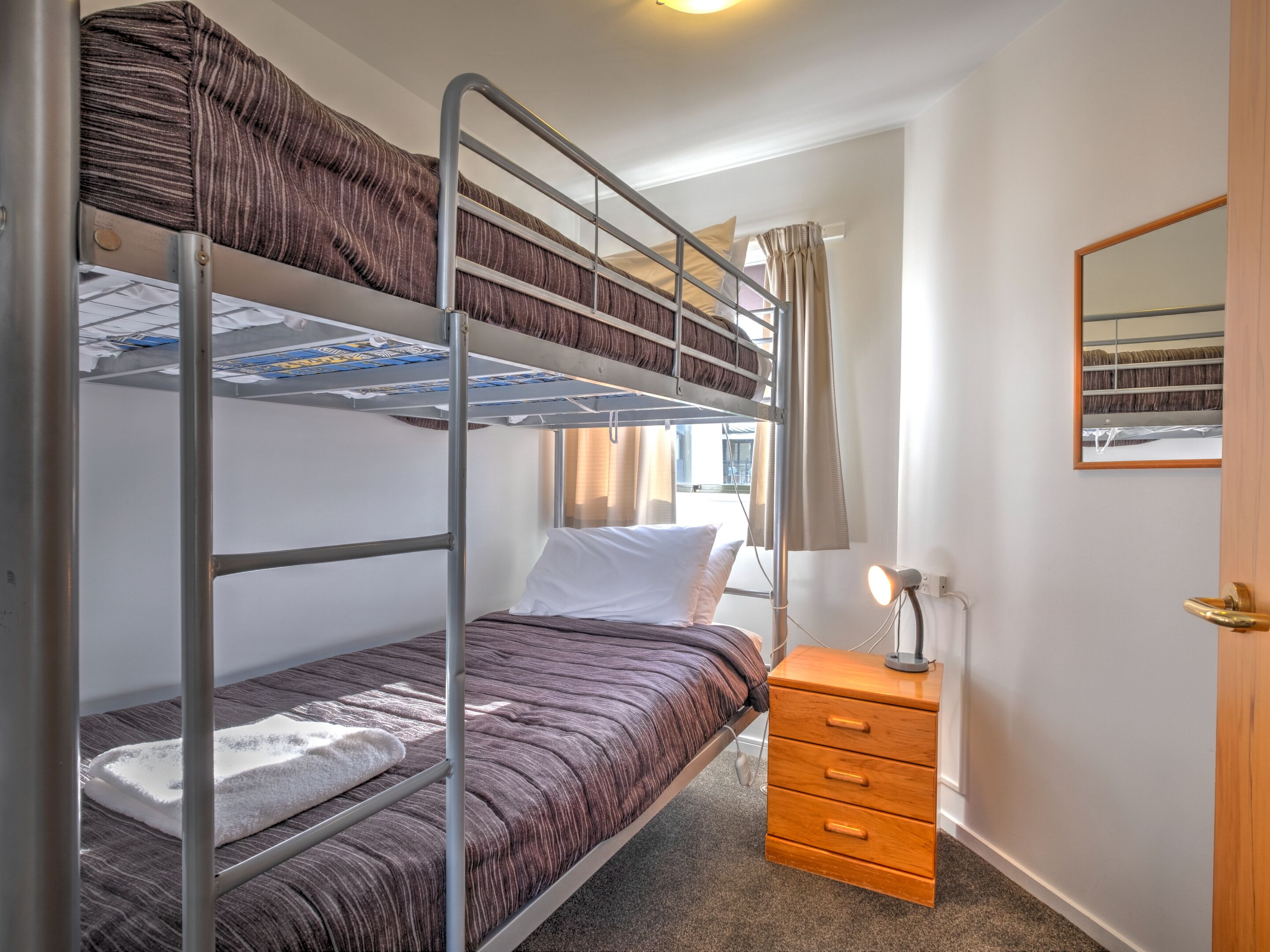 A bunk bed room with a wooden nightstand and a mirror.