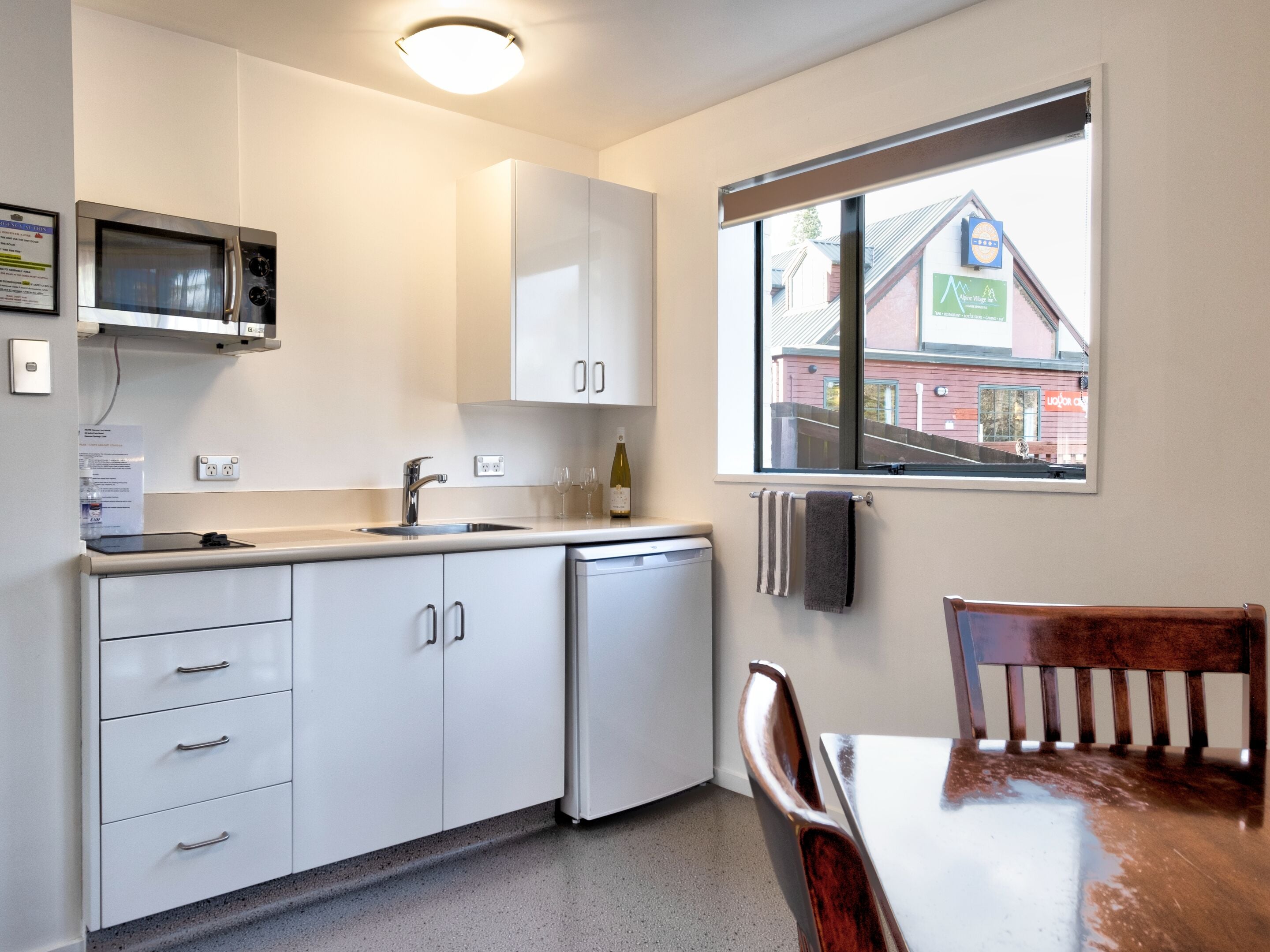 A compact kitchen with white cabinets, a built-in microwave, a sink, and a window offering a view of a building outside.