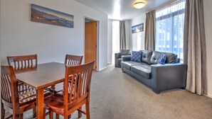 A modern living room with a dining table, chairs, a sofa, and a large window with curtains. - ASURE Hanmer Inn Motel (Hanmer Springs)