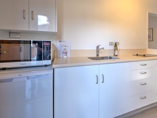 A modern kitchen with white cabinets, a built-in microwave, a sink, and a wine glass.