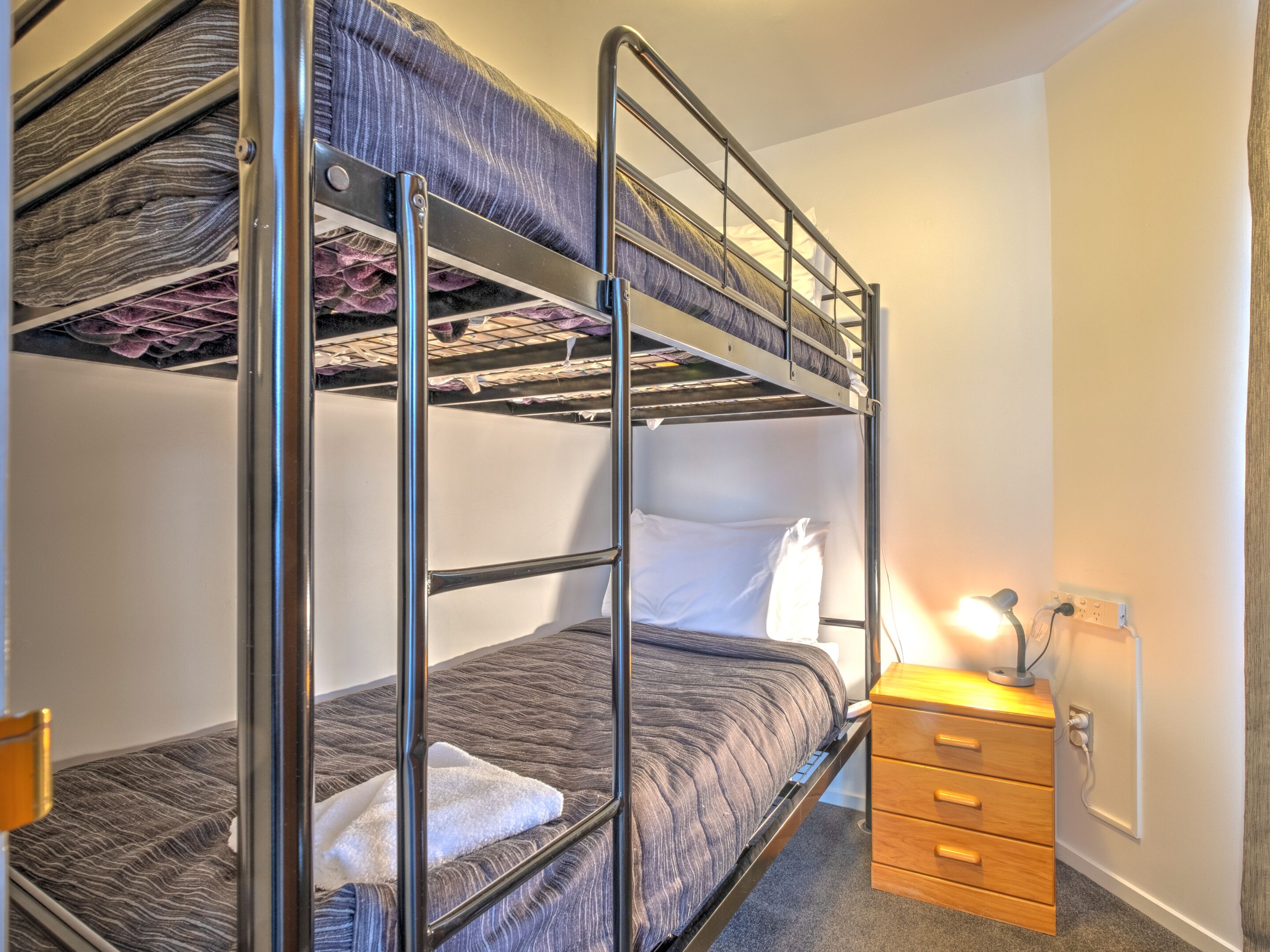 A bunk bed room with a wooden dresser and a lamp.