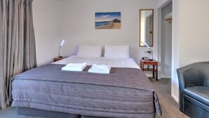 A hotel room with a large bed, a bedside table with a lamp, a chair, a painting on the wall, and a mirror. - ASURE Hanmer Inn Motel (Hanmer Springs)