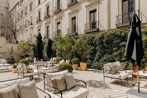 An outdoor seating area with multiple tables and chairs, surrounded by potted plants and umbrellas.