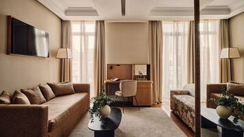 A hotel room with a sofa, a desk, a chair, and a TV.