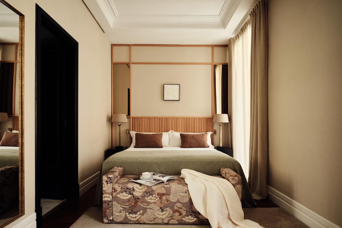 Une chambre d’hôtel avec un grand lit, une table de chevet, une commode, un miroir et une fenêtre avec des rideaux.