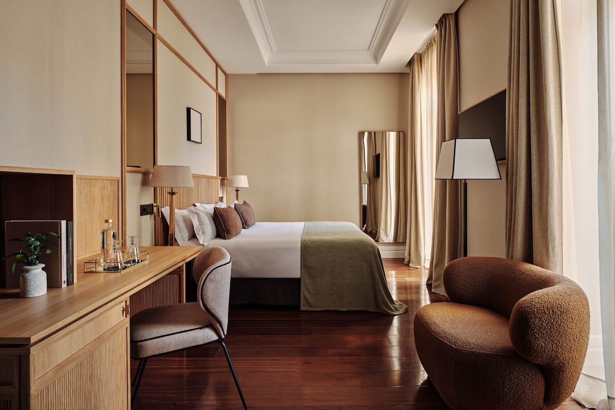 Une chambre d’hôtel comprenant un lit, des tables de chevet, un bureau avec une chaise, un canapé et un grand miroir.
