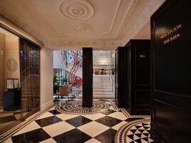 A hotel lobby with a checkered floor, a staircase, and a reception desk.