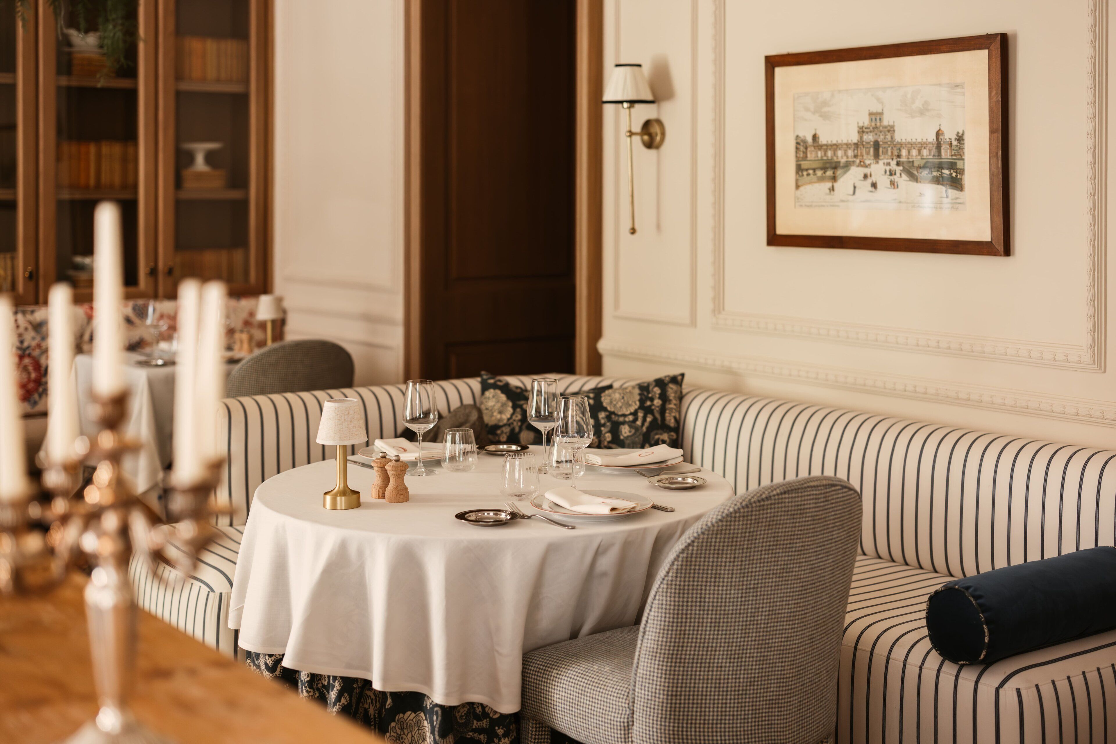 Un coin repas avec une table ronde dressée pour quatre personnes, entourée de canapés à rayures.