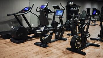 Un gimnasio con diversas máquinas de ejercicio, incluyendo cintas de correr y elípticas, dispuestas en una sala amplia con suelo de madera.