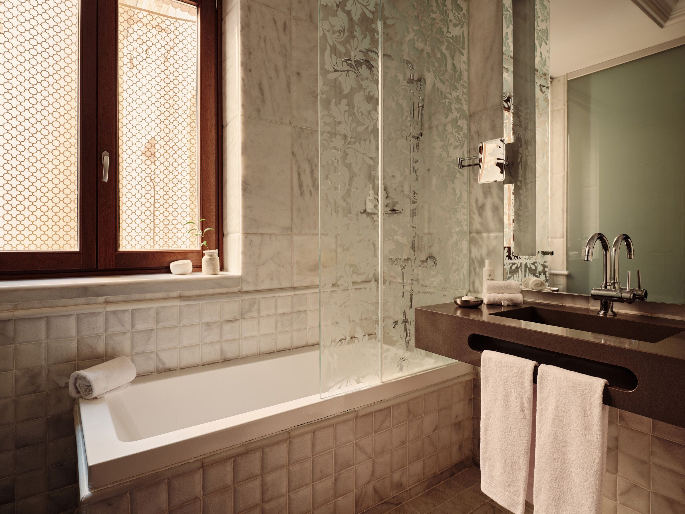 A bathroom with a bathtub, a shower, a sink with a mirror, and a window with a decorative pattern.