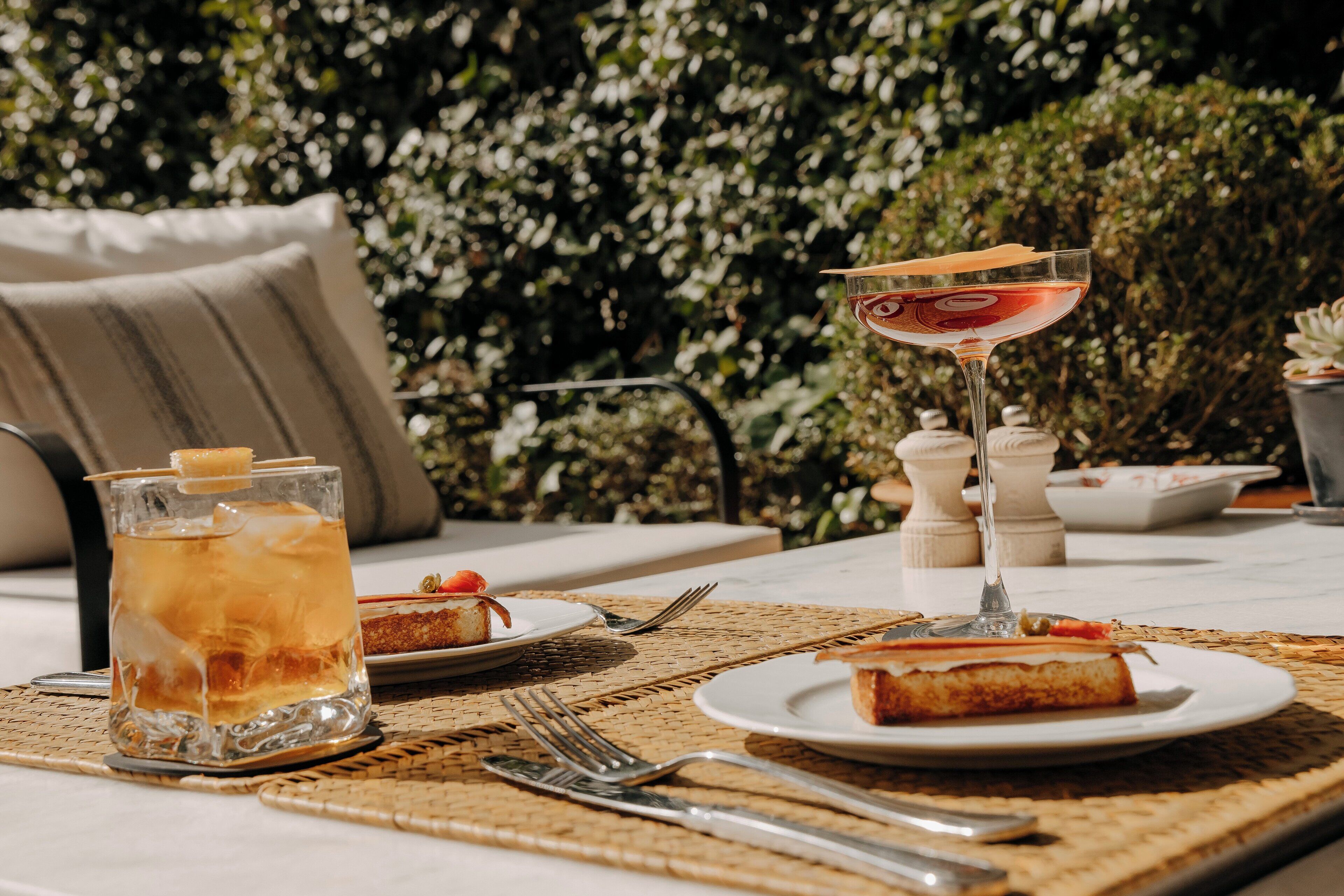 Ein Tisch ist gedeckt mit einem Glas Eisgetränk, einem Cocktailglas, Tellern mit Kuchenstücken und Besteck.