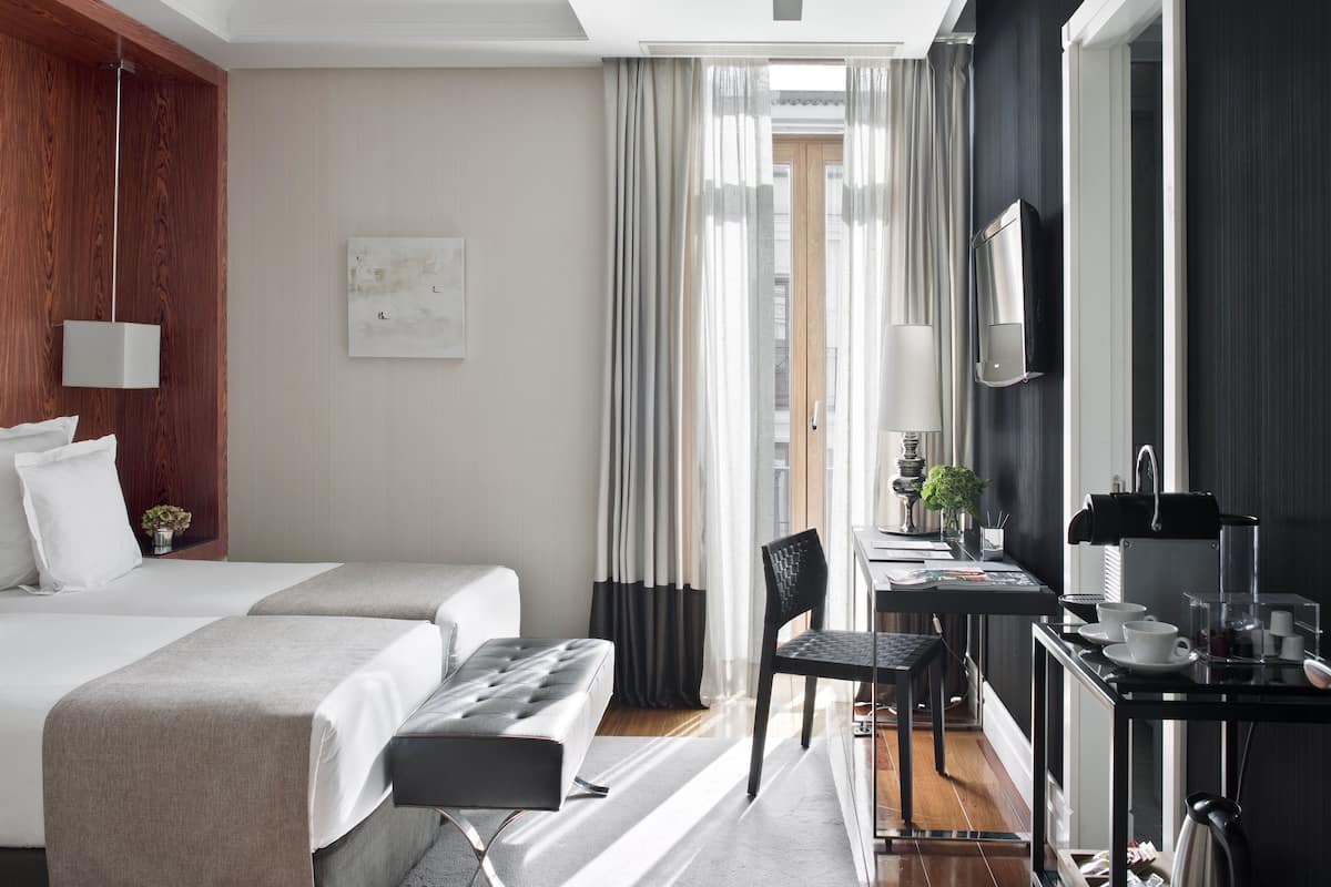 Une chambre d’hôtel avec un lit, un bureau, une chaise, une petite table et une fenêtre avec des rideaux.