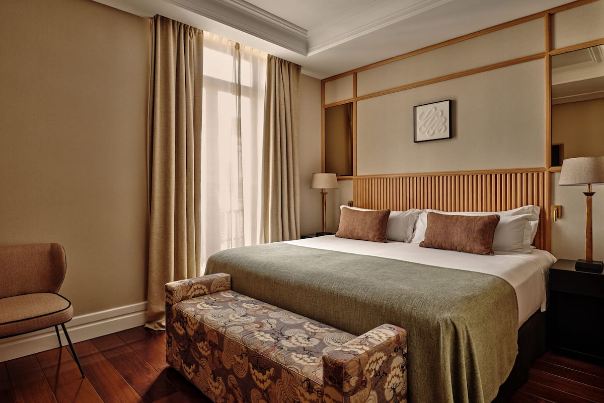 Une chambre d’hôtel avec un grand lit, un banc, une chaise et une table de chevet avec des lampes.