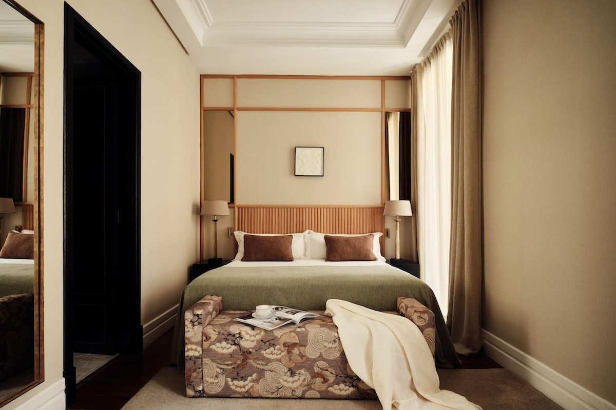 Une chambre d’hôtel avec un grand lit, une table de chevet, un miroir et une fenêtre avec des rideaux.