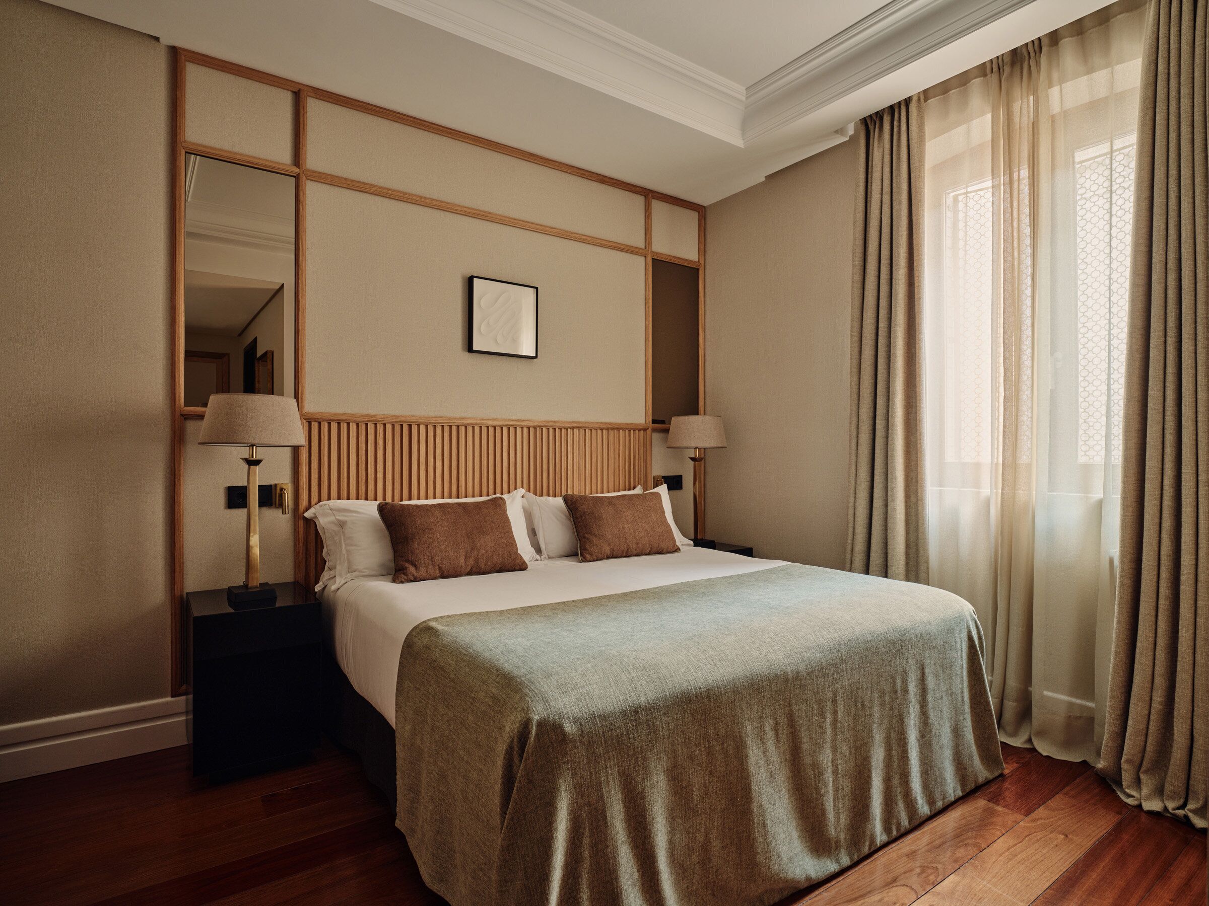 A hotel room with a large bed, a nightstand, a mirror, and a window with curtains.