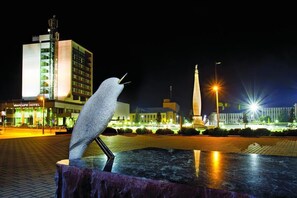 A sculpture of a bird on a pedestal in an urban square at night. - Mercure Marijampole (Marijampole)