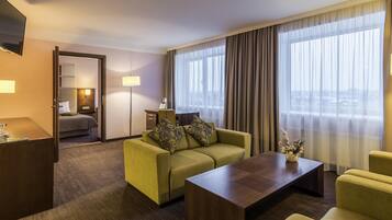 A hotel room with a bed, a sofa, a coffee table, a desk, and a TV.