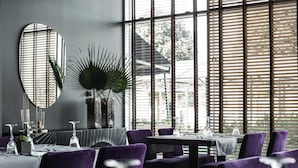 Un espace repas moderne avec des tables rondes, des chaises violettes et de grandes fenêtres équipées de stores.